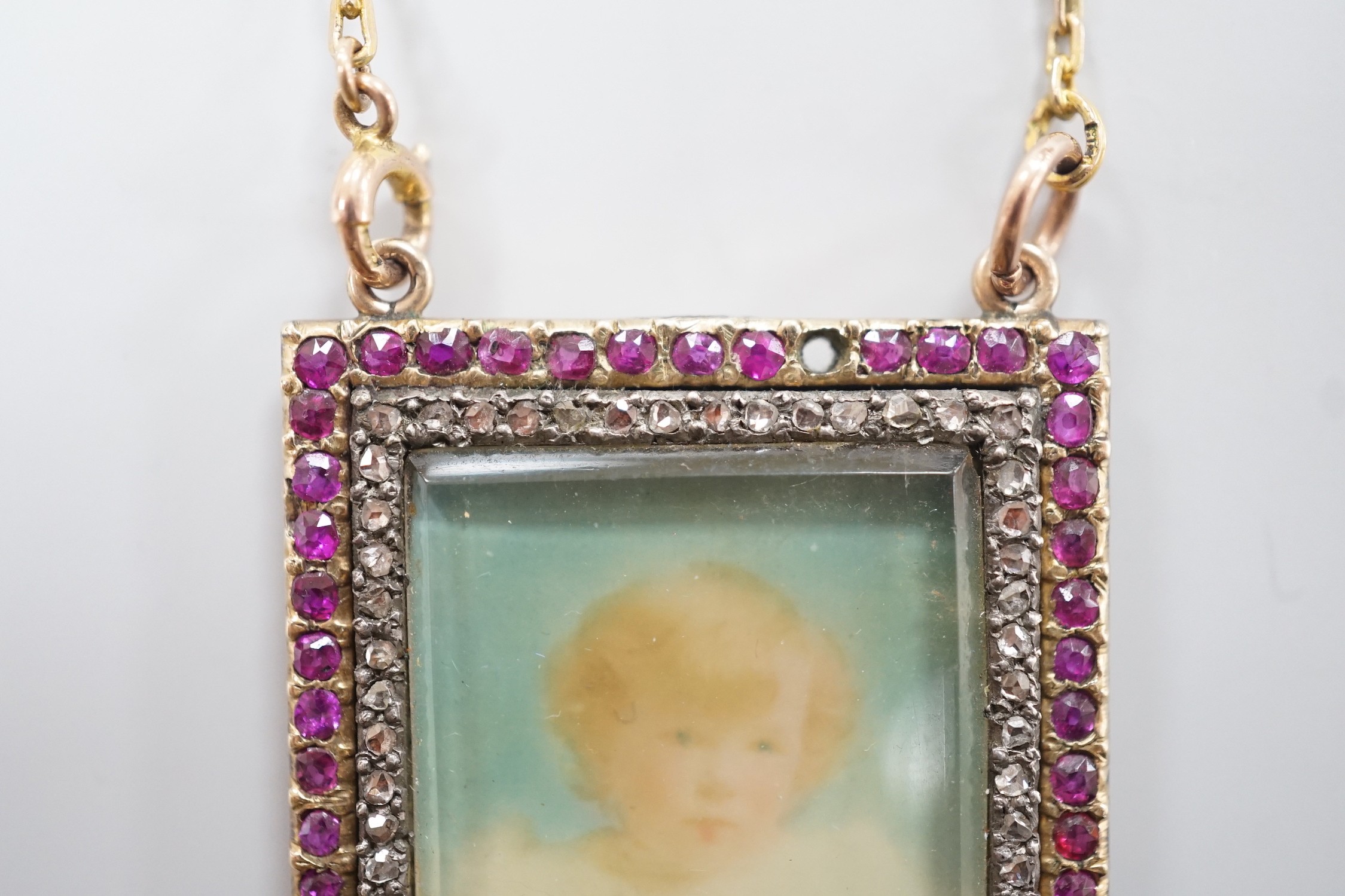 An early 20th century yellow metal, ruby and diamond mounted portrait pendant, 34mm (two rubies missing), on a 9ct chain